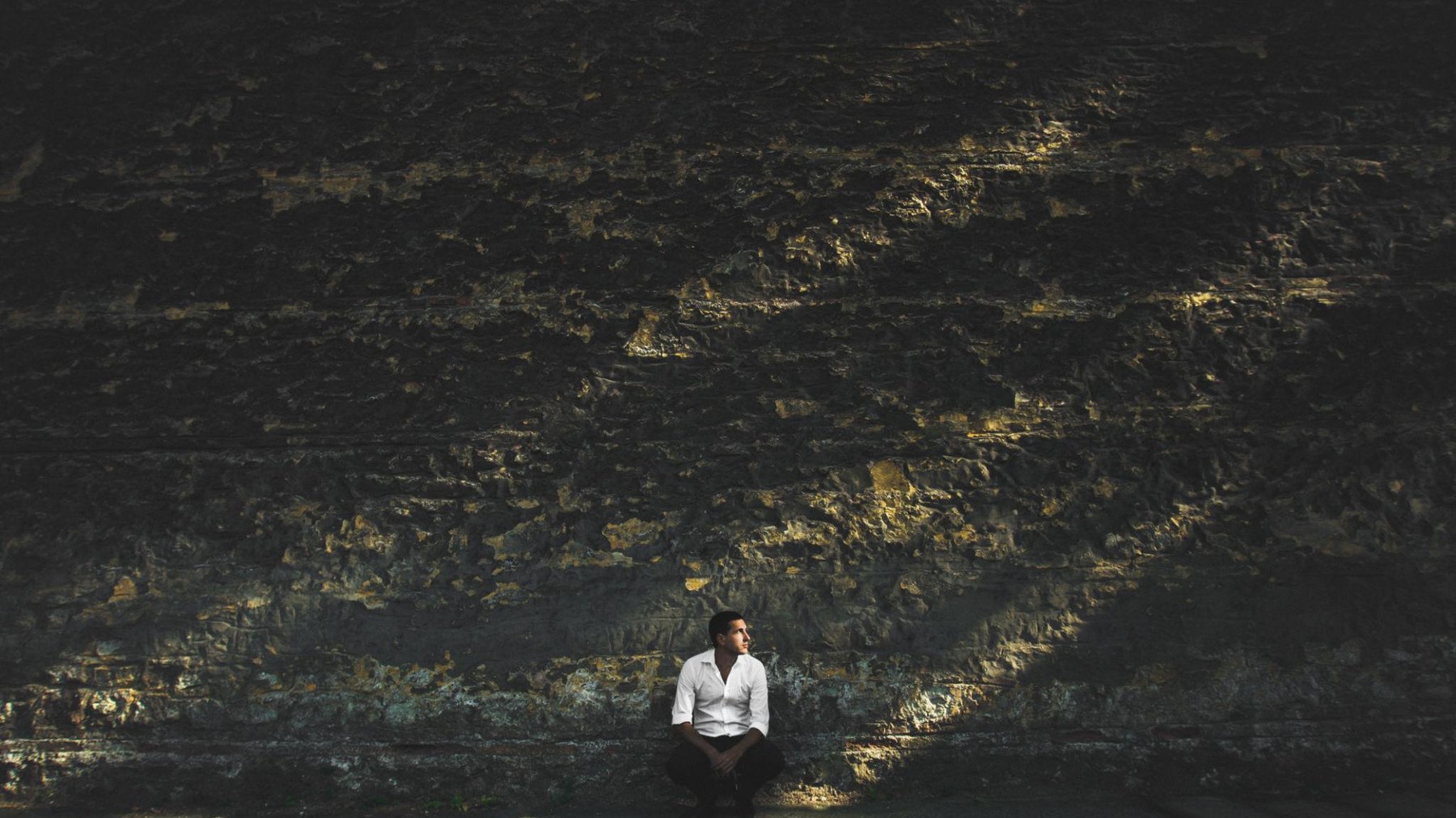 A lone figure sitting against a dark textured wall