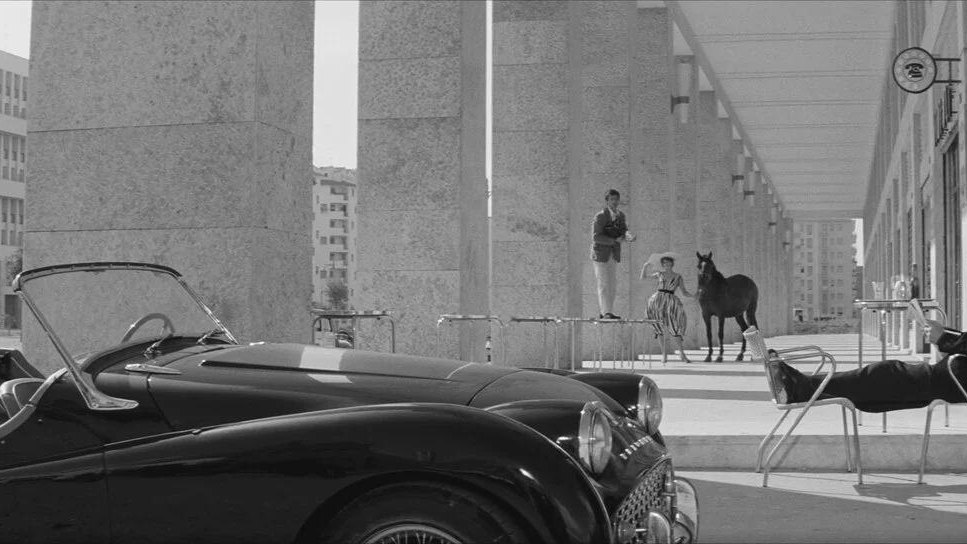 Black-and-white Italian cinema scene with a sports car and modernist architecture